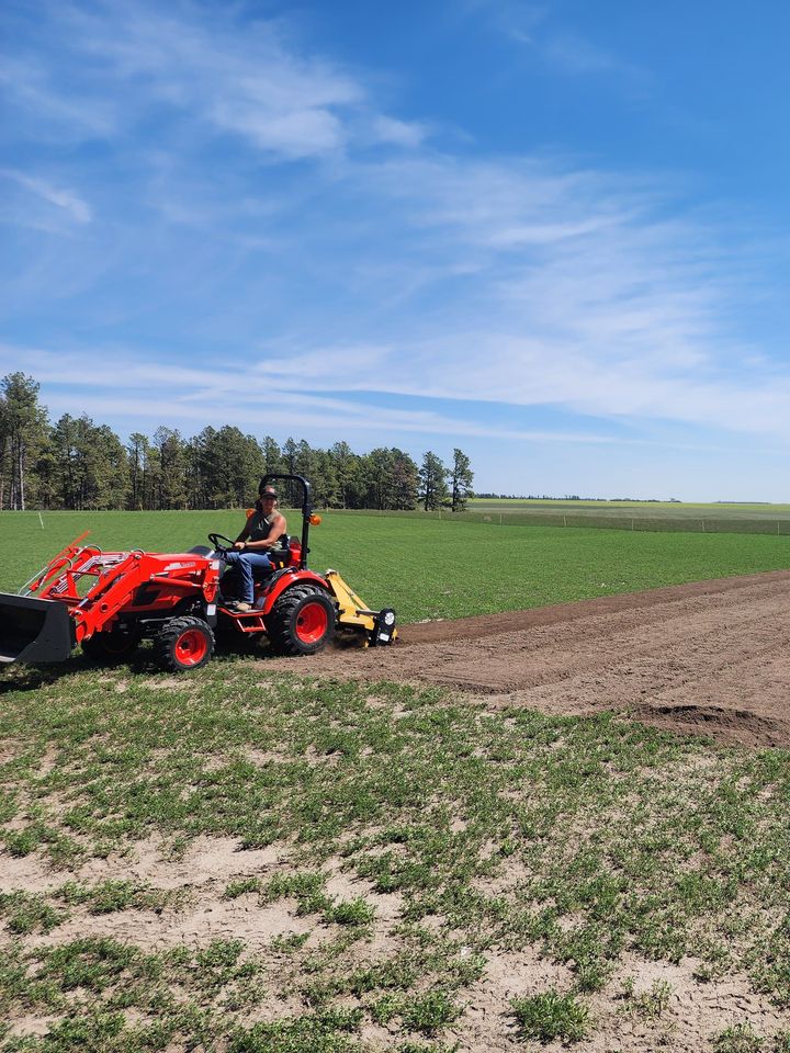 An orange tractor with a tiller working the field, half still green and half freshly tilled