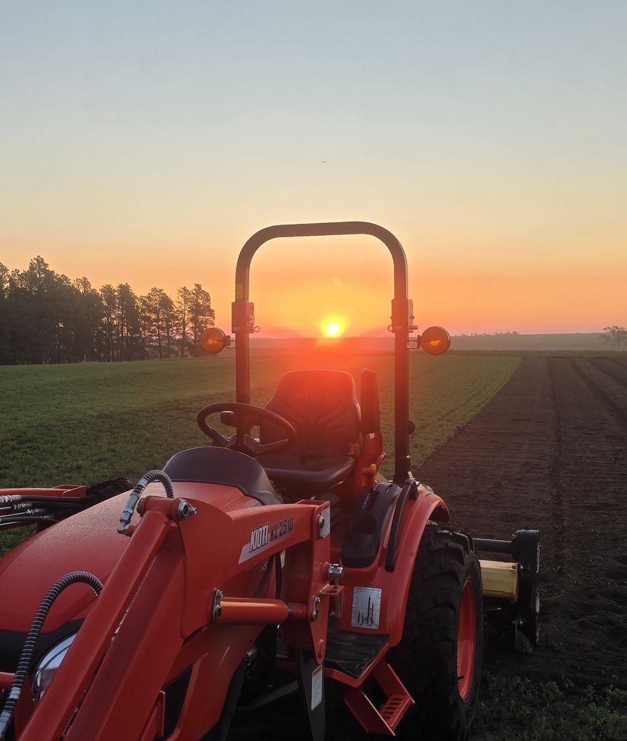 Sunrise over the MUG field, seen through the frame of an orange tractor beside freshly prepared rows