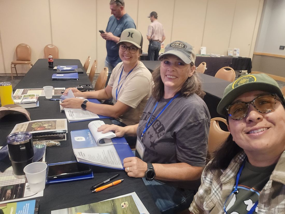Three MUG team members smiling at a table covered with workbooks during a soil health training